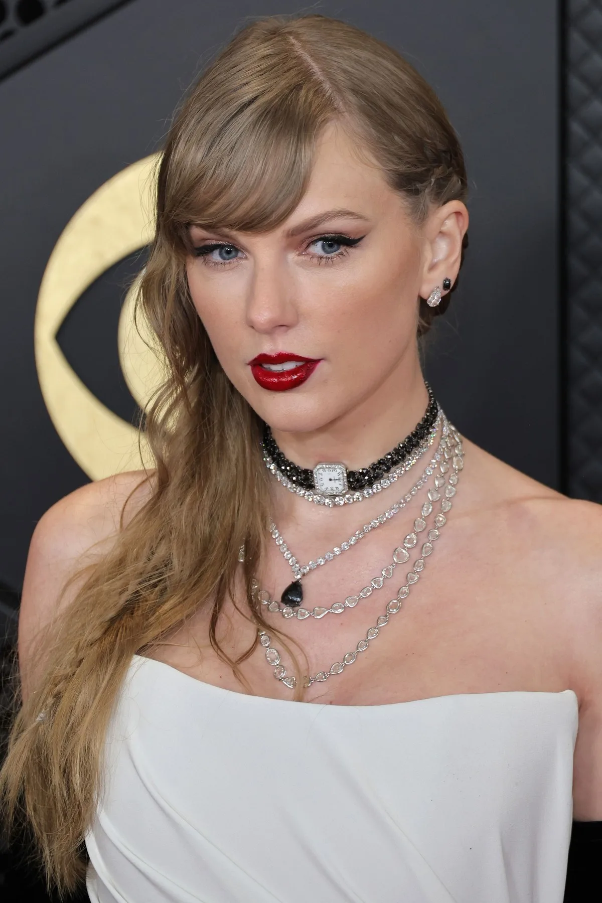 Close portrait of Taylor Swift with a watch choker, layered necklaces, a braid and red lipstick