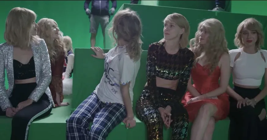Taylor Swift sitting with costumed stand-ins on green-screen steps, including the Junior Jewels outfit and a silver jacket