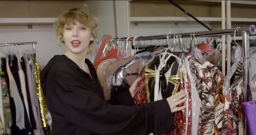 Taylor Swift holding the red sequined ringmaster jacket with black lapels and gold trim