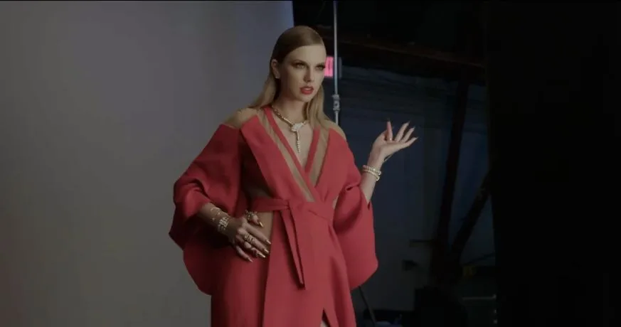 Taylor Swift wearing a loose red robe and layered jewelry on the music video set